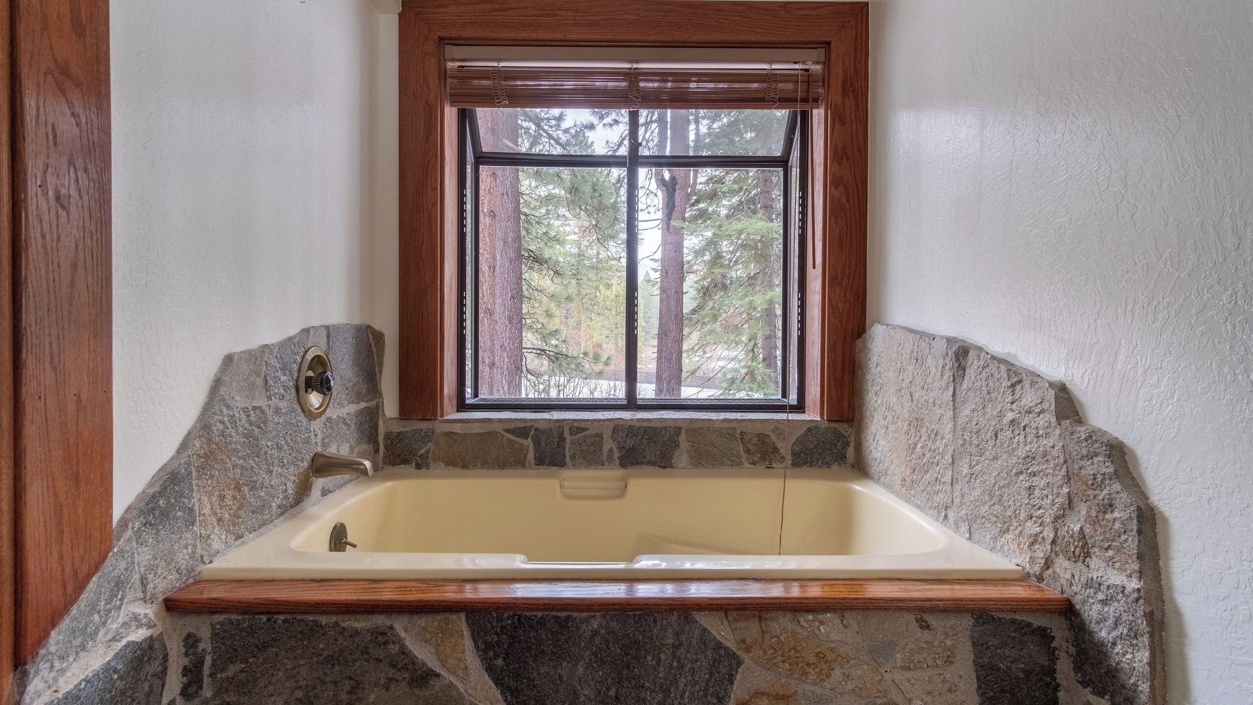 Une salle de bain avec un mur en pierre, une fenêtre en bois et une baignoire.