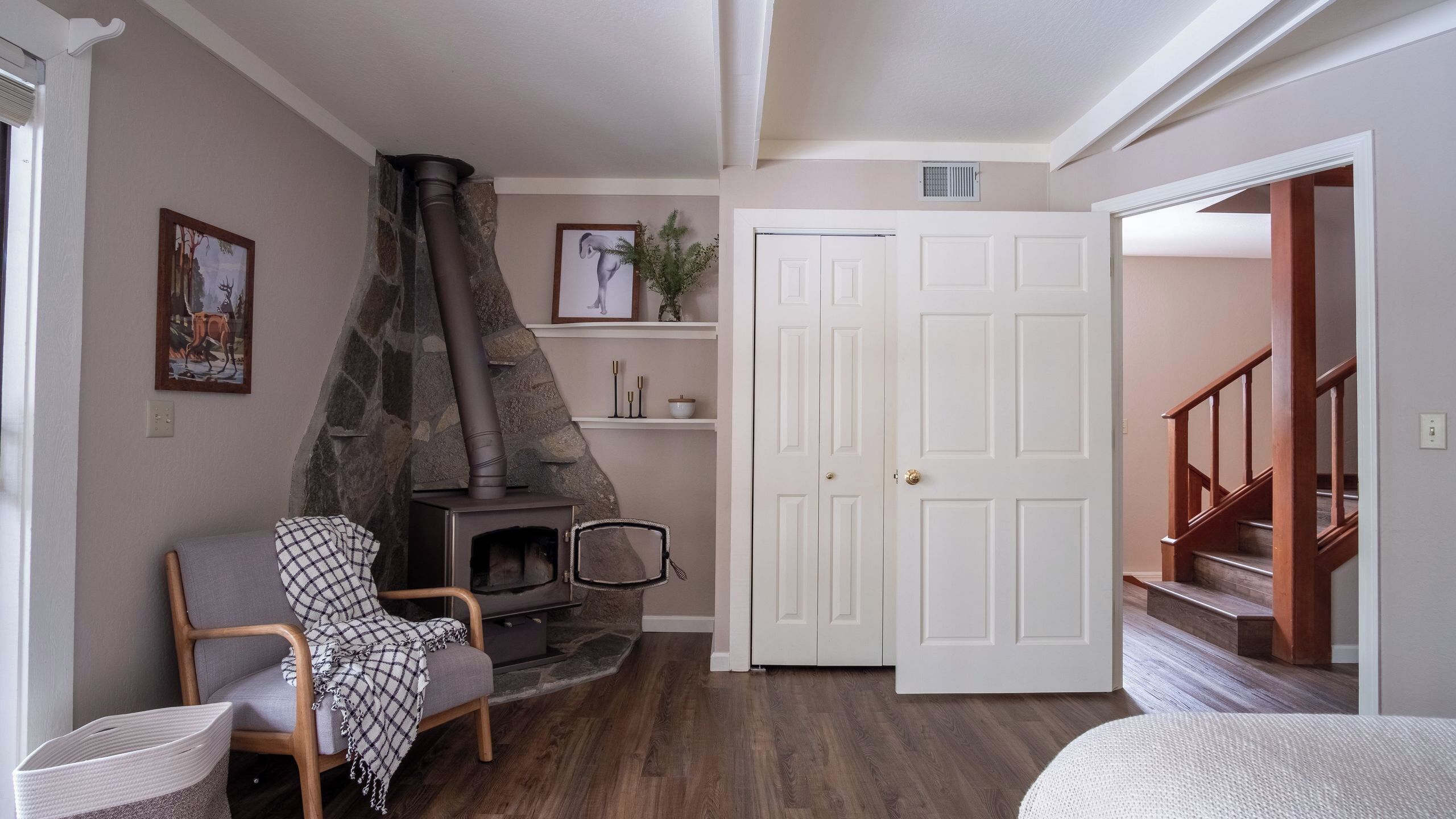 A cozy living room with a stone fireplace, a wooden chair, a white door, and a staircase.