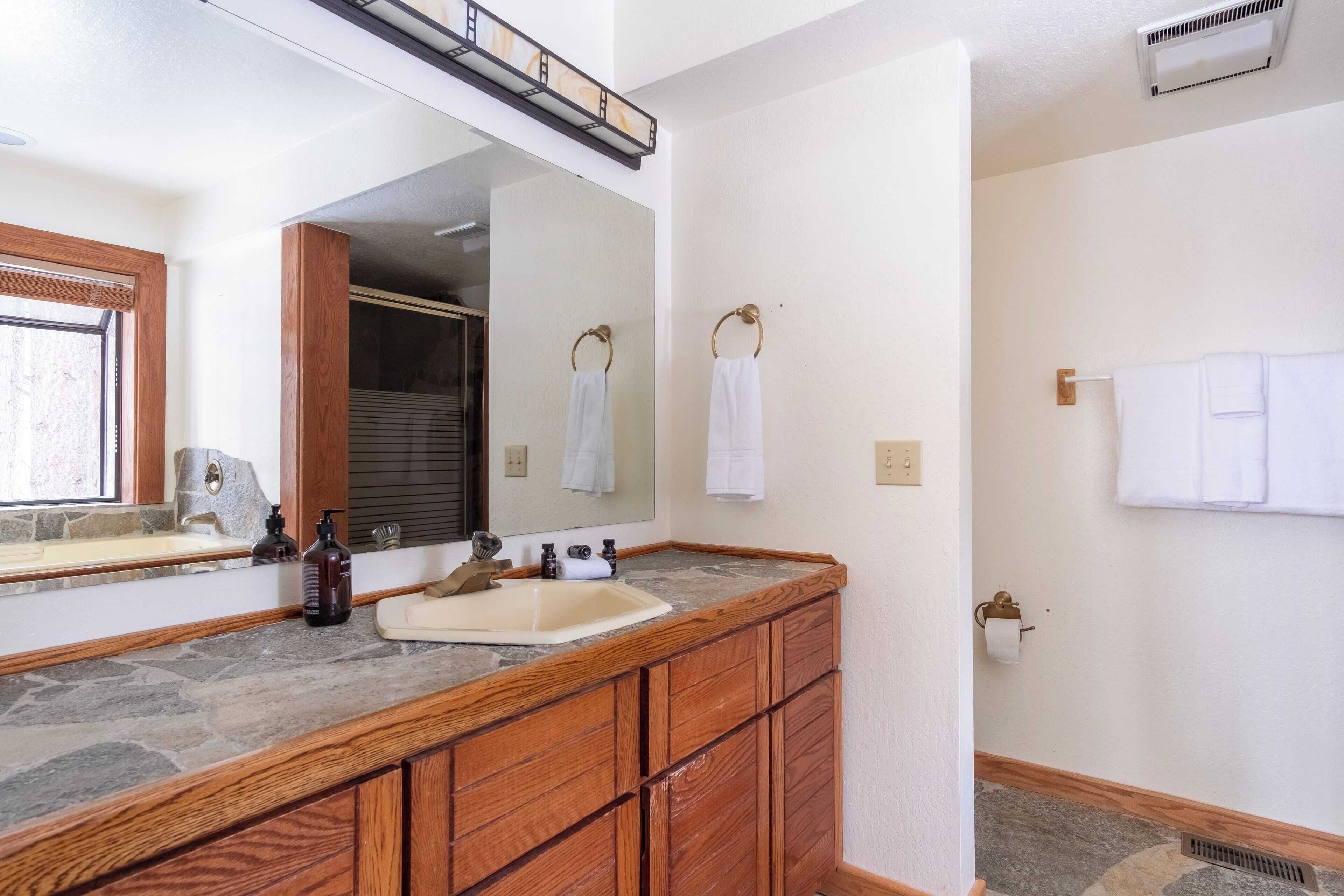 Une salle de bain avec un comptoir en pierre, des meubles en bois, un miroir et un espace douche.