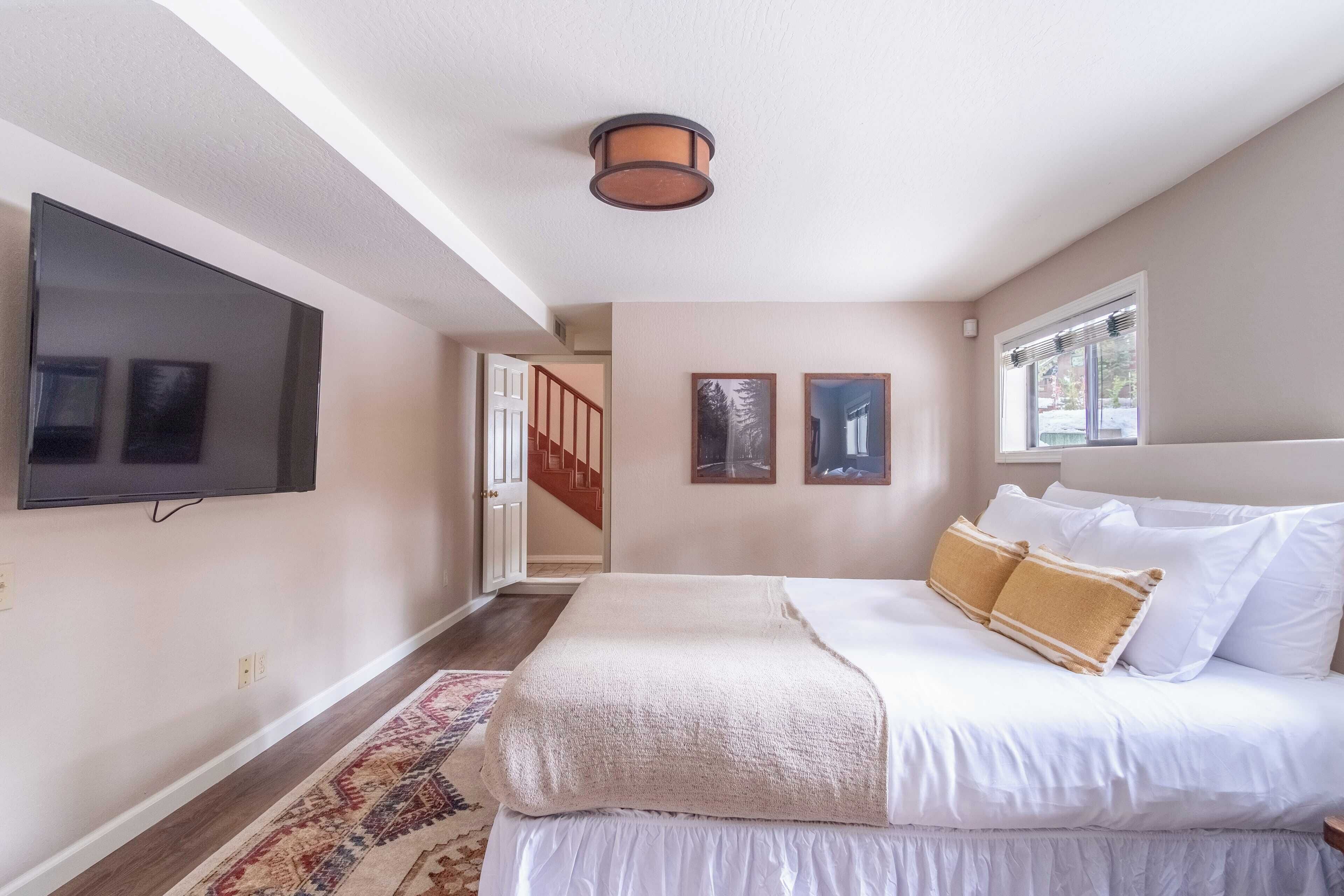 Un dormitorio con una cama, un televisor montado en la pared y una ventana con persianas.