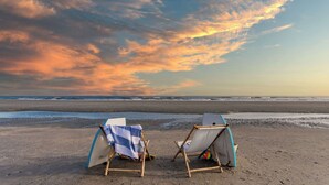 Twee strandstoelen met parasols op een zandstrand, gericht op de oceaan.