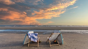 Two beach chairs with umbrellas on a sandy beach, facing the ocean.