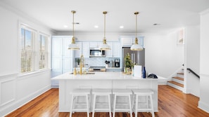 A kitchen with white cabinetry, a central island with bar stools, stainless steel appliances, and pendant lighting.