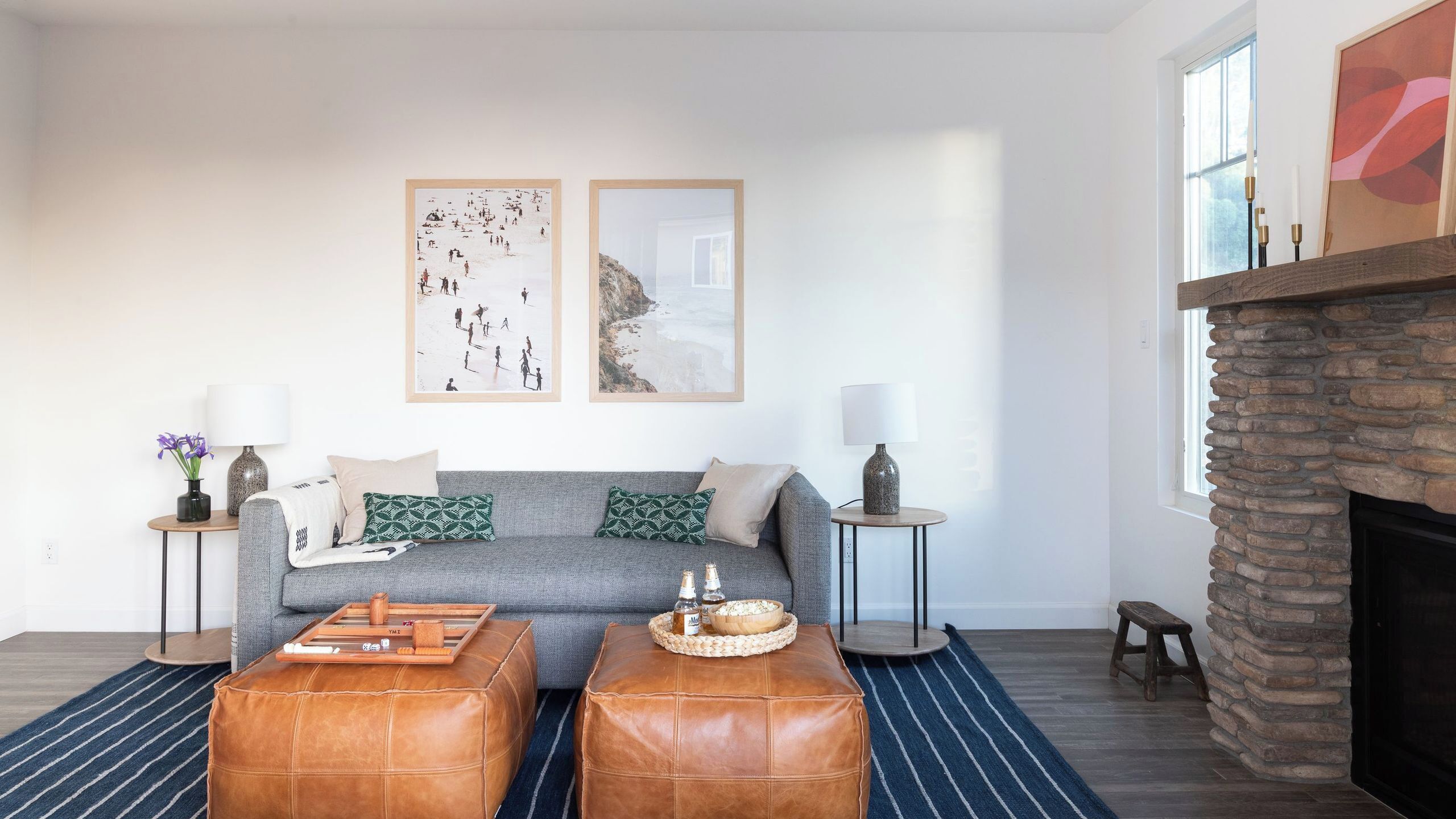 A living room with a grey sofa, two leather ottomans, a fireplace, and two framed pictures on the wall.