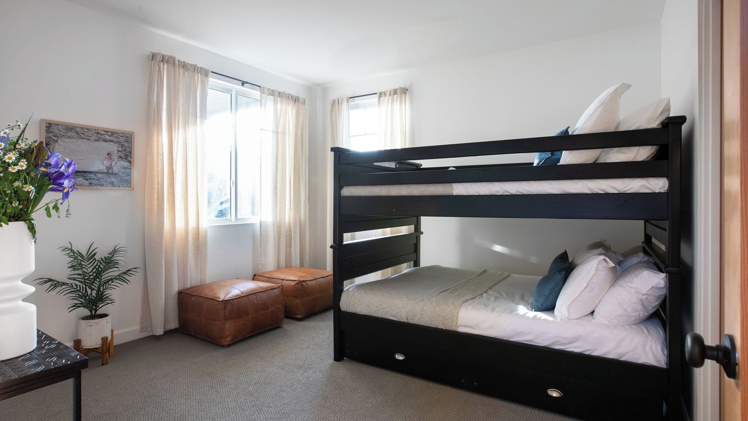 Une chambre avec un lit superposé, une fenêtre, des rideaux, une plante en pot et une petite table.