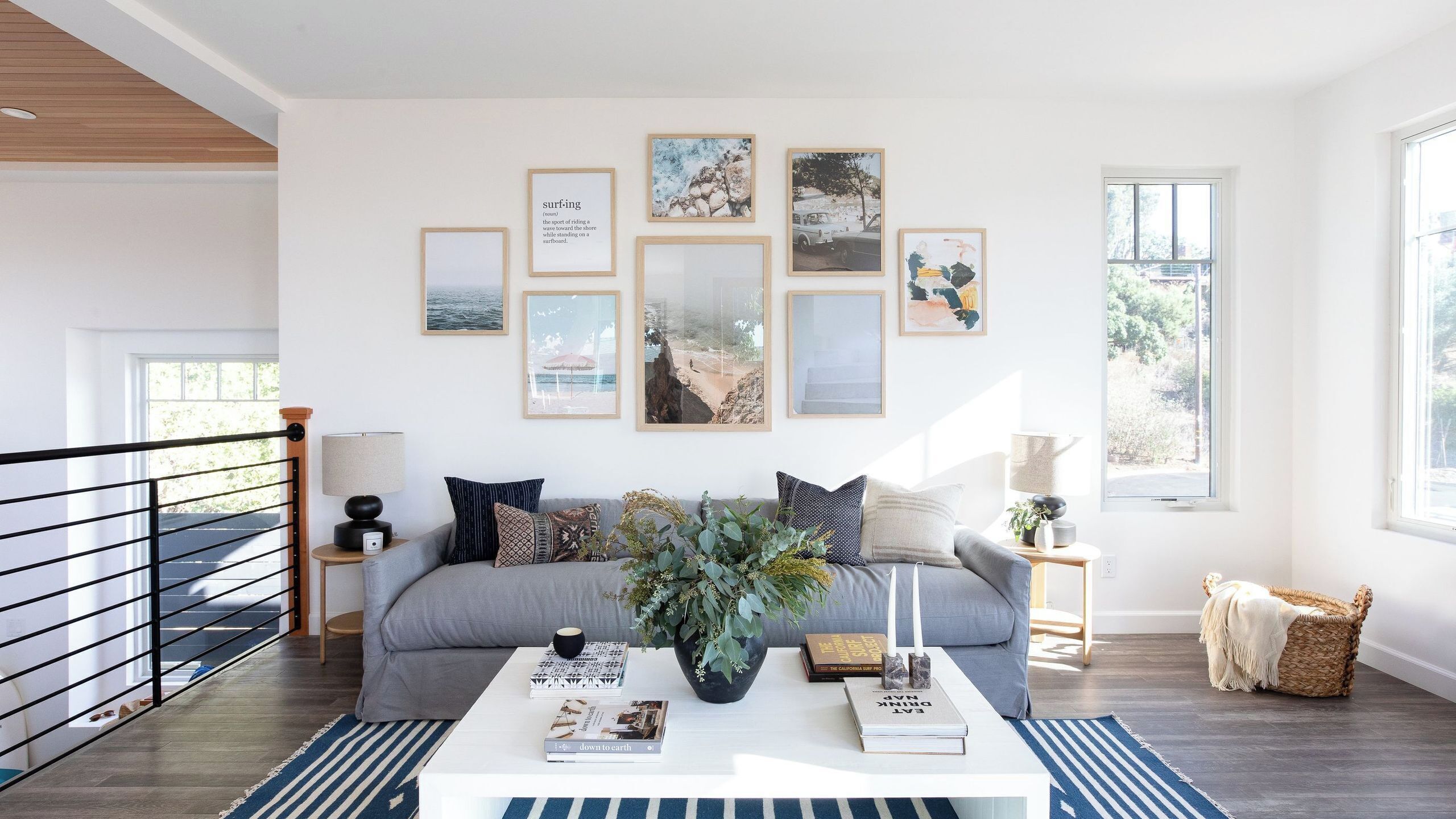 Una sala de estar moderna con un sofá gris, una mesa de centro con libros y un florero, y cuadros en la pared.