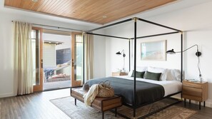 A bedroom with a four-poster bed, a nightstand, a bedside lamp, a window with curtains, and a view of the outdoors.