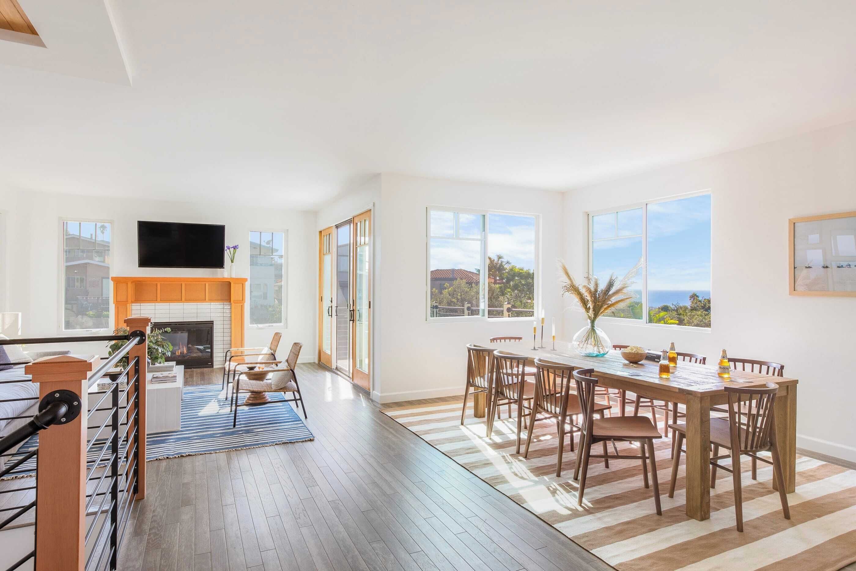 A spacious living area with a fireplace, a dining table, and large windows offering a view of the outdoors.