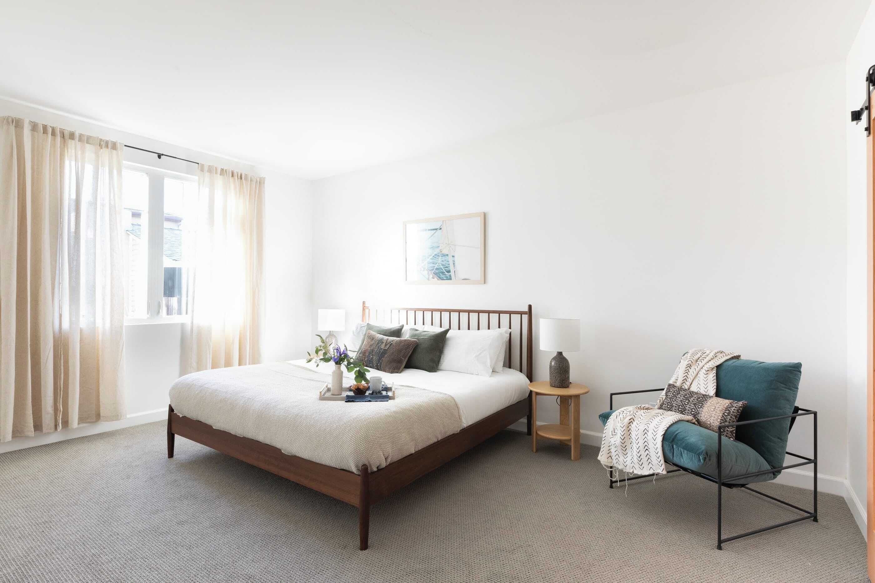 A bedroom with a wooden bed, a chair, a bedside table, and a window with curtains.