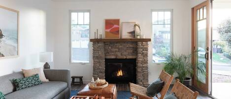 Una sala de estar con chimenea de piedra, un sofá, una mesa de centro y dos sillones de mimbre.