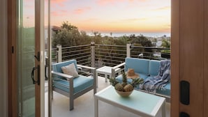 Un balcone con vista sul tramonto, un tavolo con una ciotola di ananas e mobili bianchi e blu.