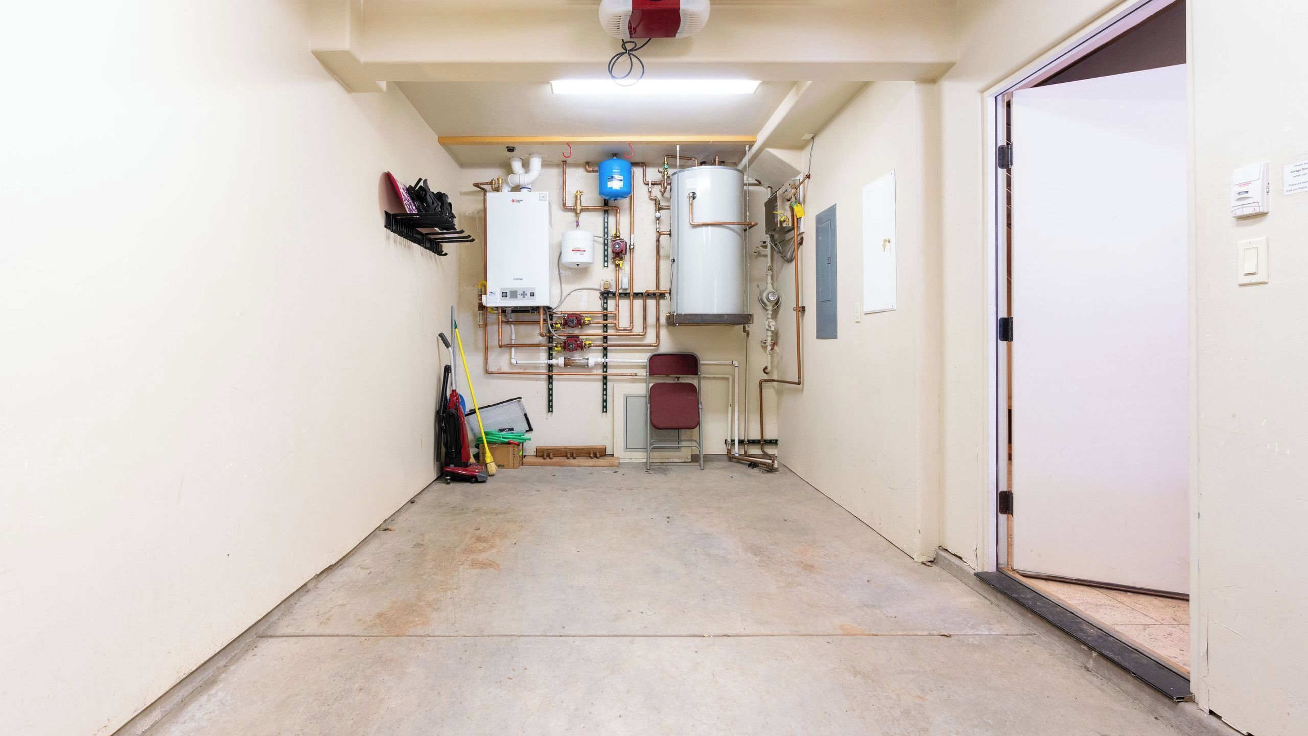 A hallway with a water heater, pipes, and a chair.