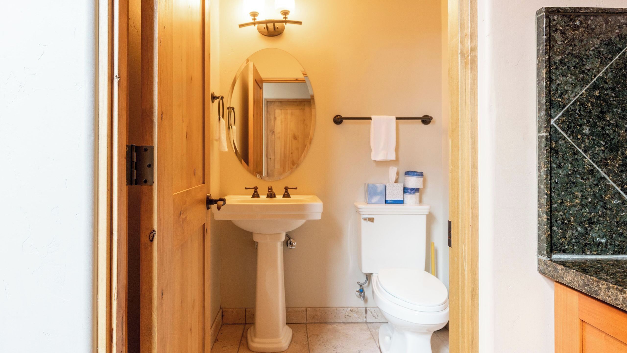 Une salle de bain avec une porte en bois, un lavabo blanc doté de trois robinets, un miroir, des toilettes et un porte-serviettes avec une serviette.