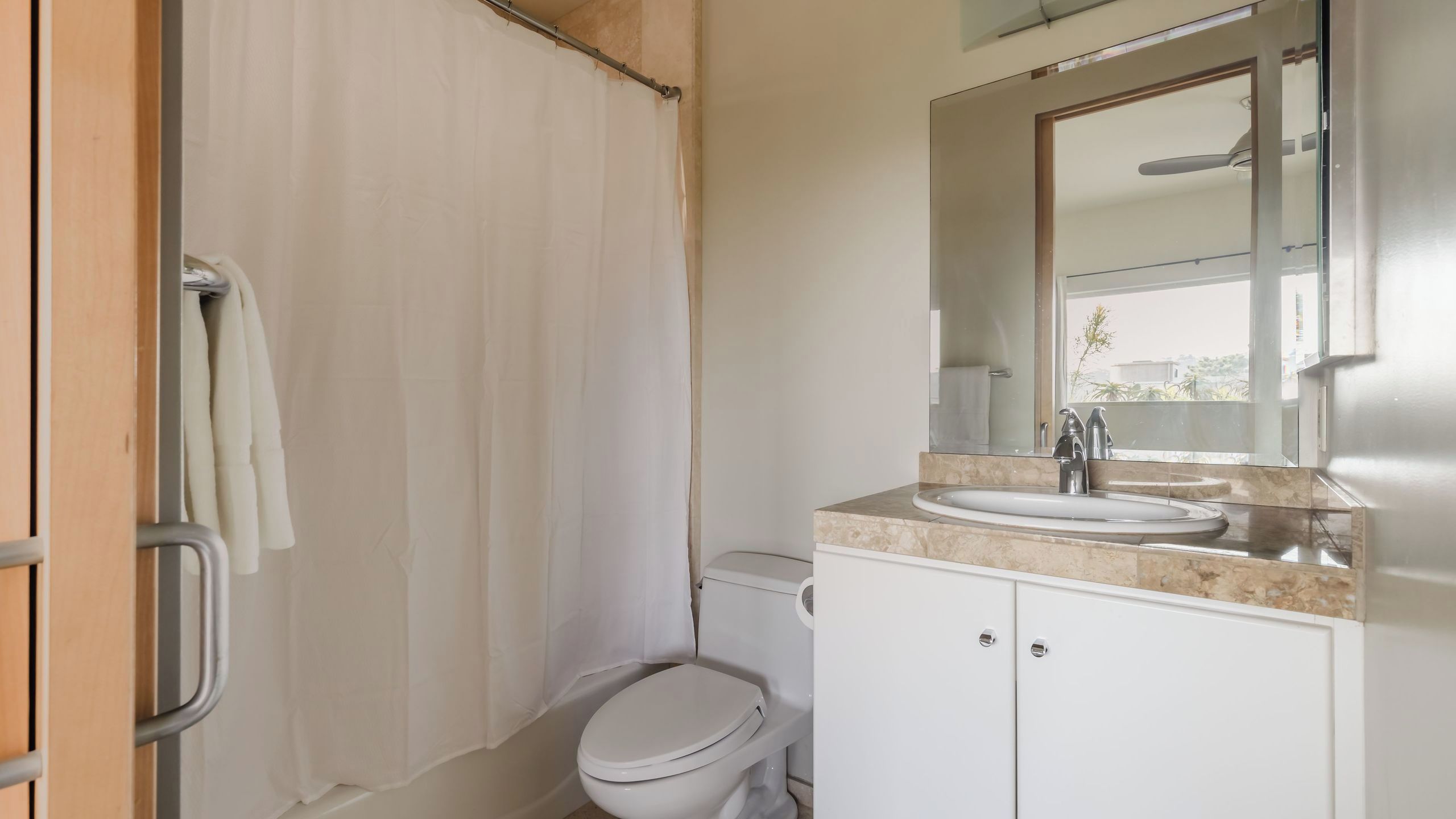 A bathroom with a toilet, a sink, a mirror, and a shower curtain.