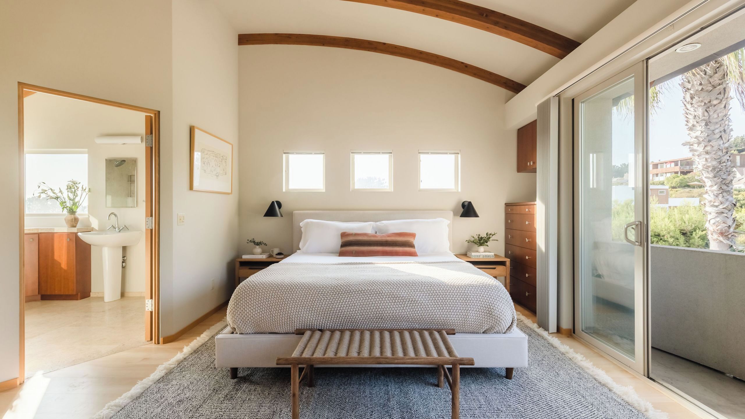 A bedroom with a bed, bedside tables, a window, a bathroom, and a balcony.