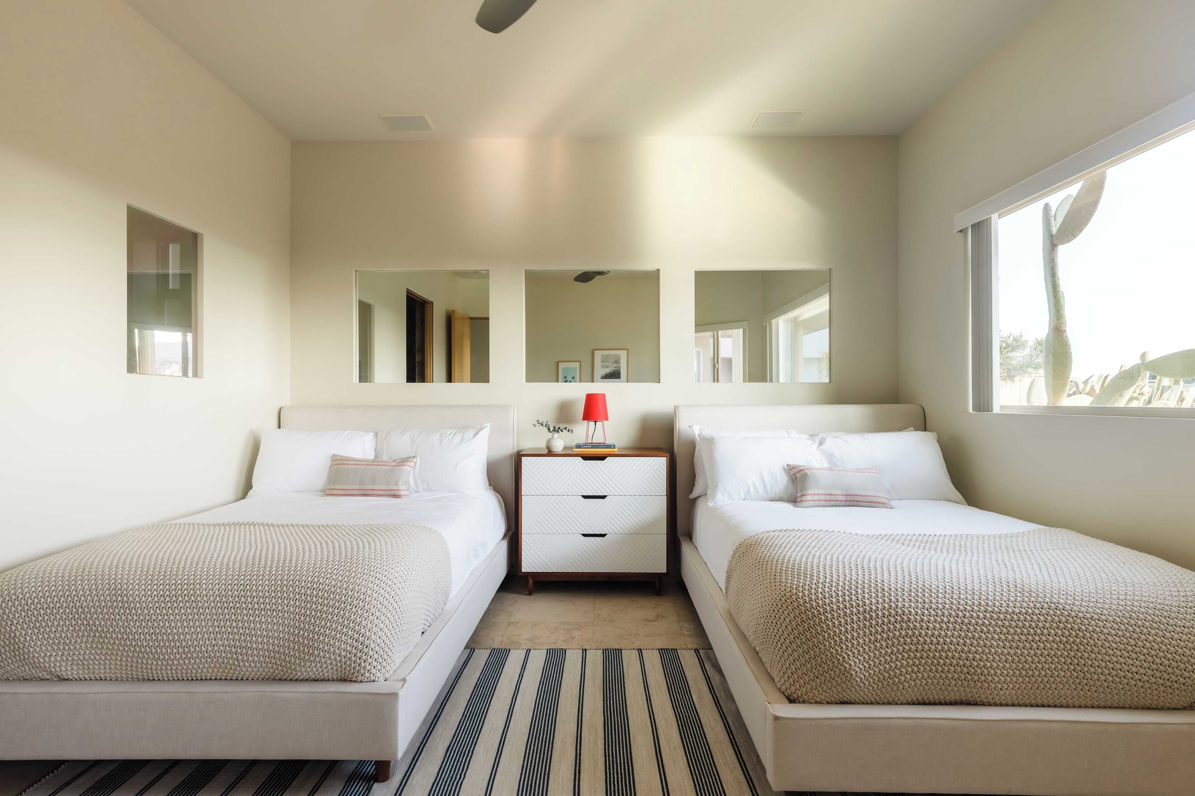 A modern bedroom with two beds, a nightstand, and a large window.