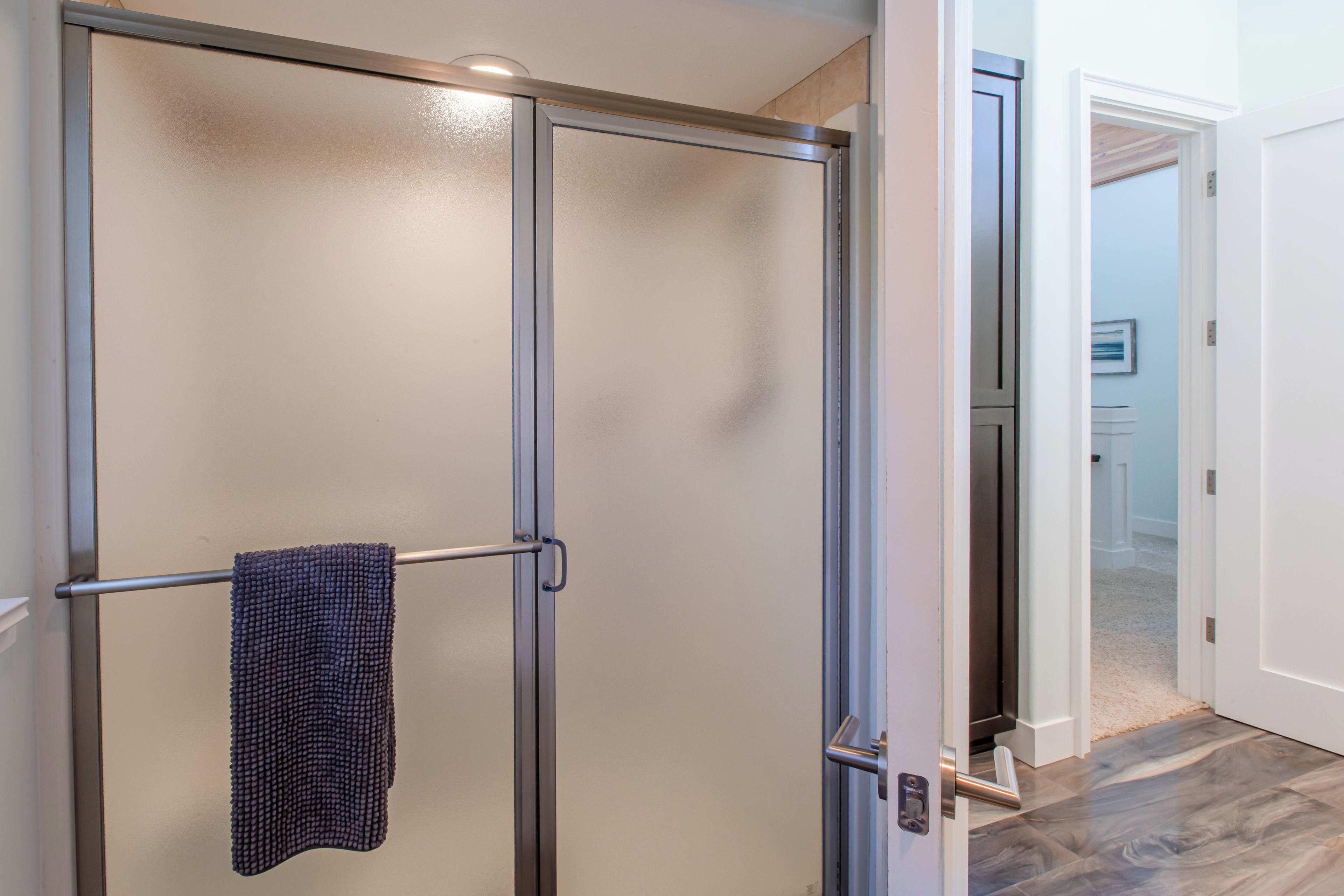 A bathroom with a glass shower enclosure, a towel rack with a towel, and a wooden floor.