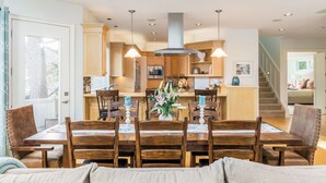 A spacious dining area with a wooden table and chairs, a kitchen in the background, and a staircase leading to another level. - Villa Manzanita by Avantstay Hot Tub, 1 Block to Beach/town, Chef's Kitchen (Manzanita)
