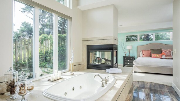 A spacious bedroom with a large window, a fireplace, and a separate bathroom with a bathtub. - Villa Manzanita by Avantstay Hot Tub, 1 Block to Beach/town, Chef's Kitchen (Manzanita)