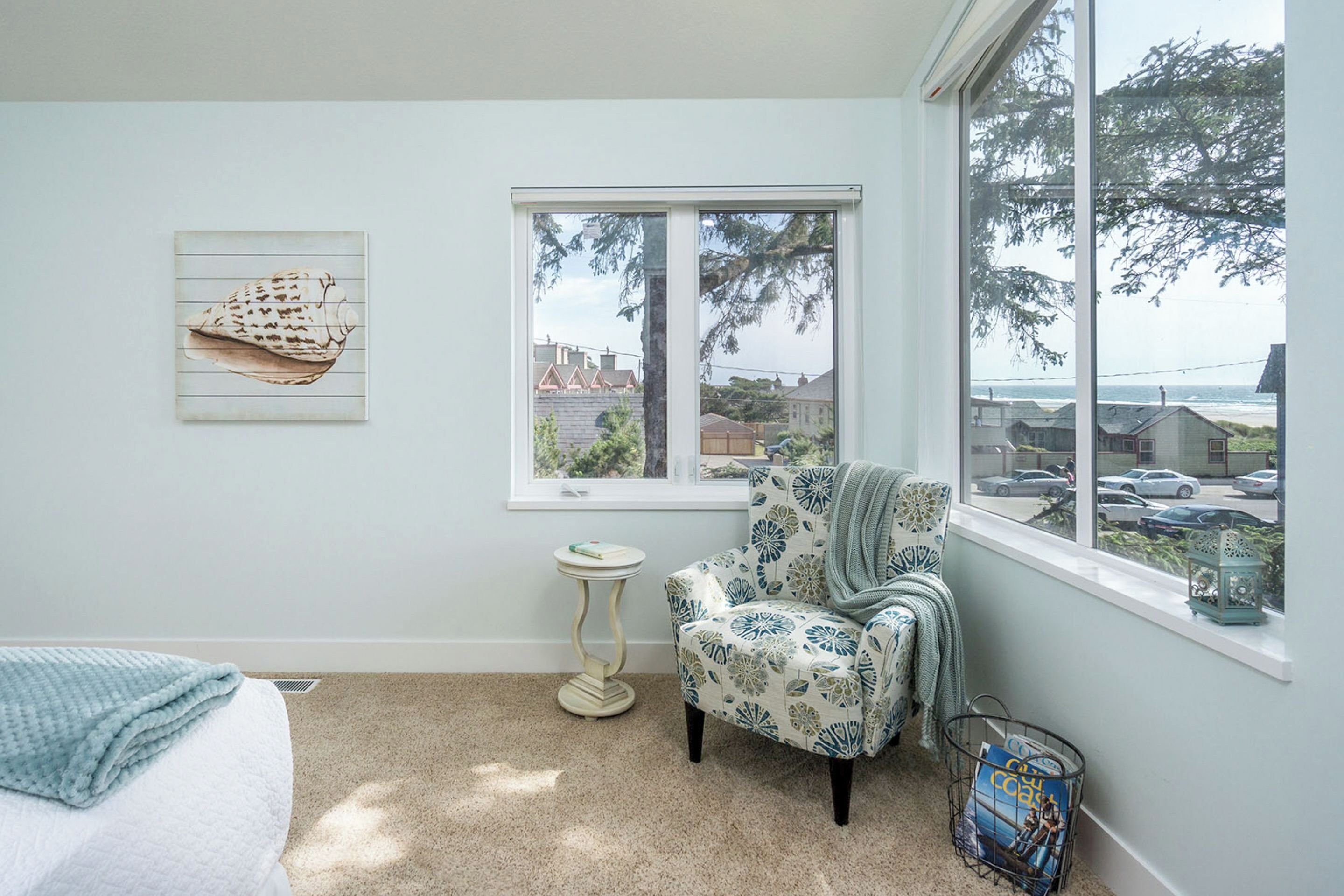 A bedroom with a bed, a chair, a window with a view of the sea, and a wall art piece.