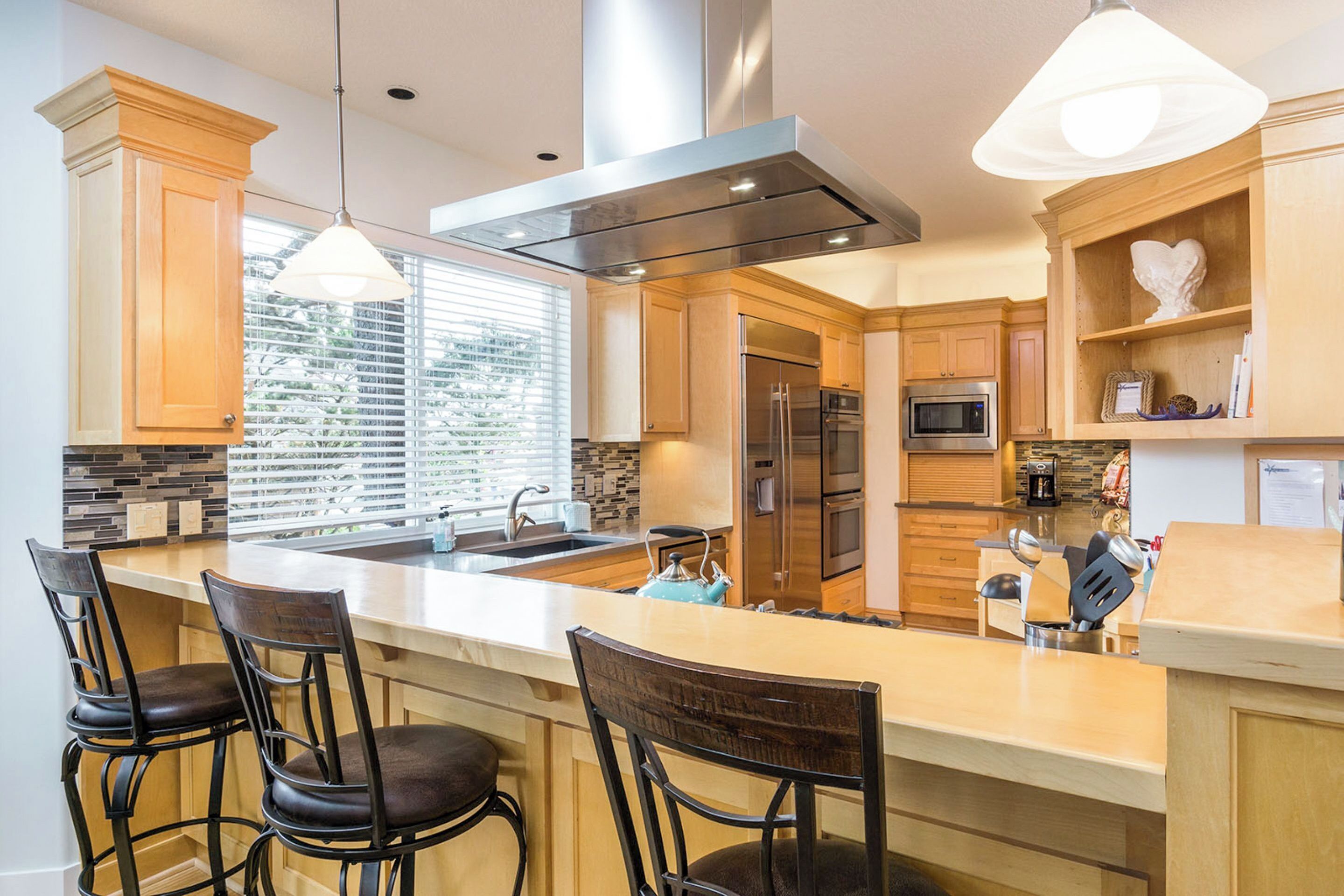 Una cocina moderna con una isla grande, taburetes de bar, electrodomésticos de acero inoxidable y vistas al exterior.