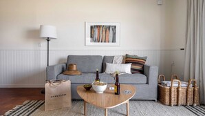 A living room with a grey sofa, a coffee table with a bowl and bottles, a lamp, and wicker baskets. - Bay View II by Avantstay Ocean View Mission Beach Home on the Sand! (San Diego)