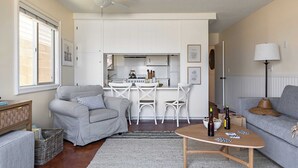 A compact living space with a kitchenette, a grey sofa, a dining area with white chairs, and a ceiling fan. - Bay View II by Avantstay Ocean View Mission Beach Home on the Sand! (San Diego)