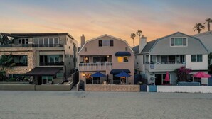 A beachfront property with a two-story house featuring a balcony, a patio with umbrellas, and a beach view. - Bay View II by Avantstay Ocean View Mission Beach Home on the Sand! (San Diego)