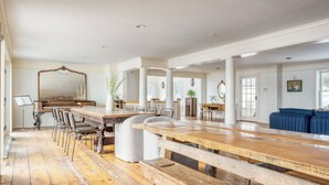A spacious room with a long wooden table, multiple chairs, a piano, and a large mirror.