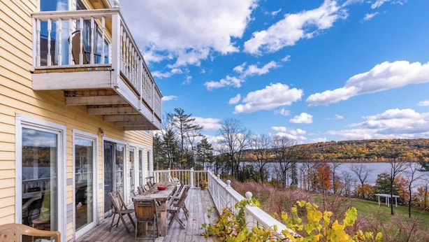 A wooden deck with outdoor furniture, a dining table, and a view of a lake and forest.