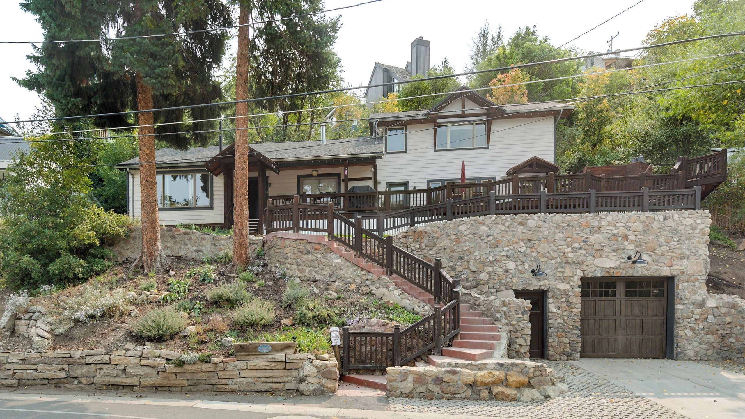 A two-story house with a stone staircase leading to a wooden deck.