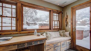 A cozy room with a wooden desk, a cushioned bench, and large windows with a snowy view. - Hillside Overlook by Avantstay Quiet Mountain Getaway w/ Incredible Views! (Park City)
