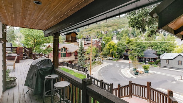 A wooden deck with outdoor seating, a covered grill, and a view of a street with houses and a stop sign. - Hillside Overlook by Avantstay Quiet Mountain Getaway w/ Incredible Views! (Park City)