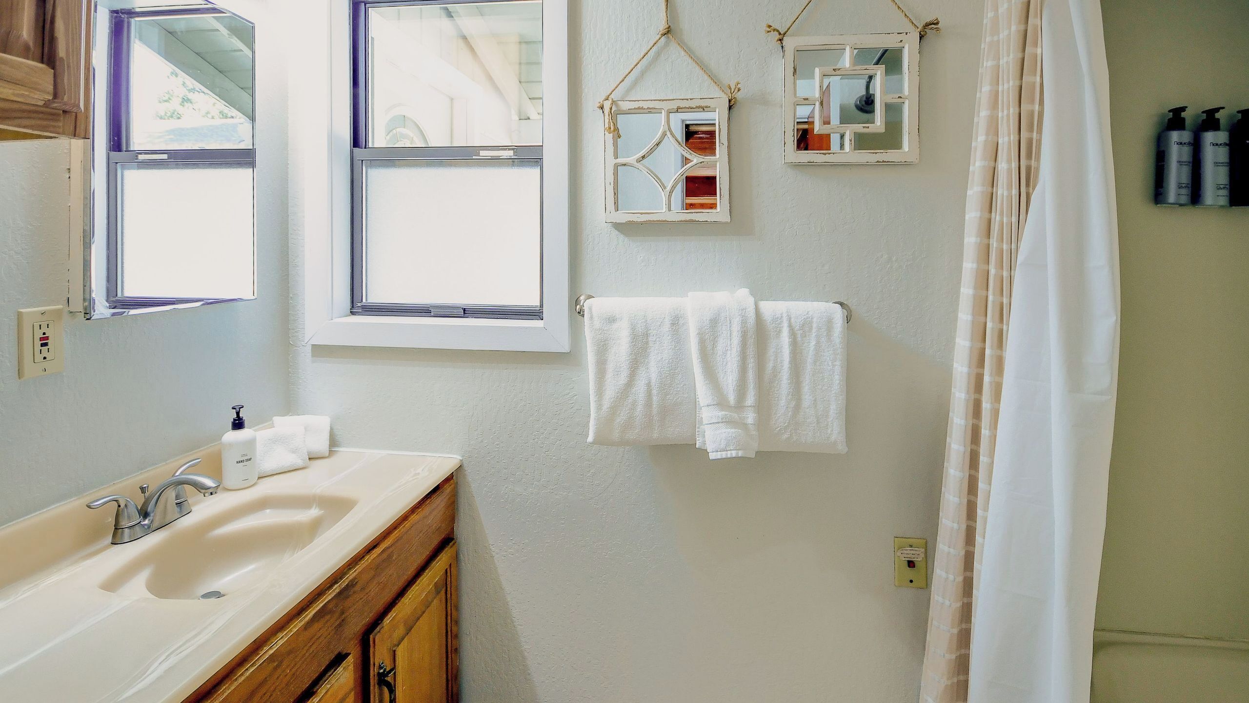 Un baño con lavamanos, dos ventanas, espejo y cortina de ducha.