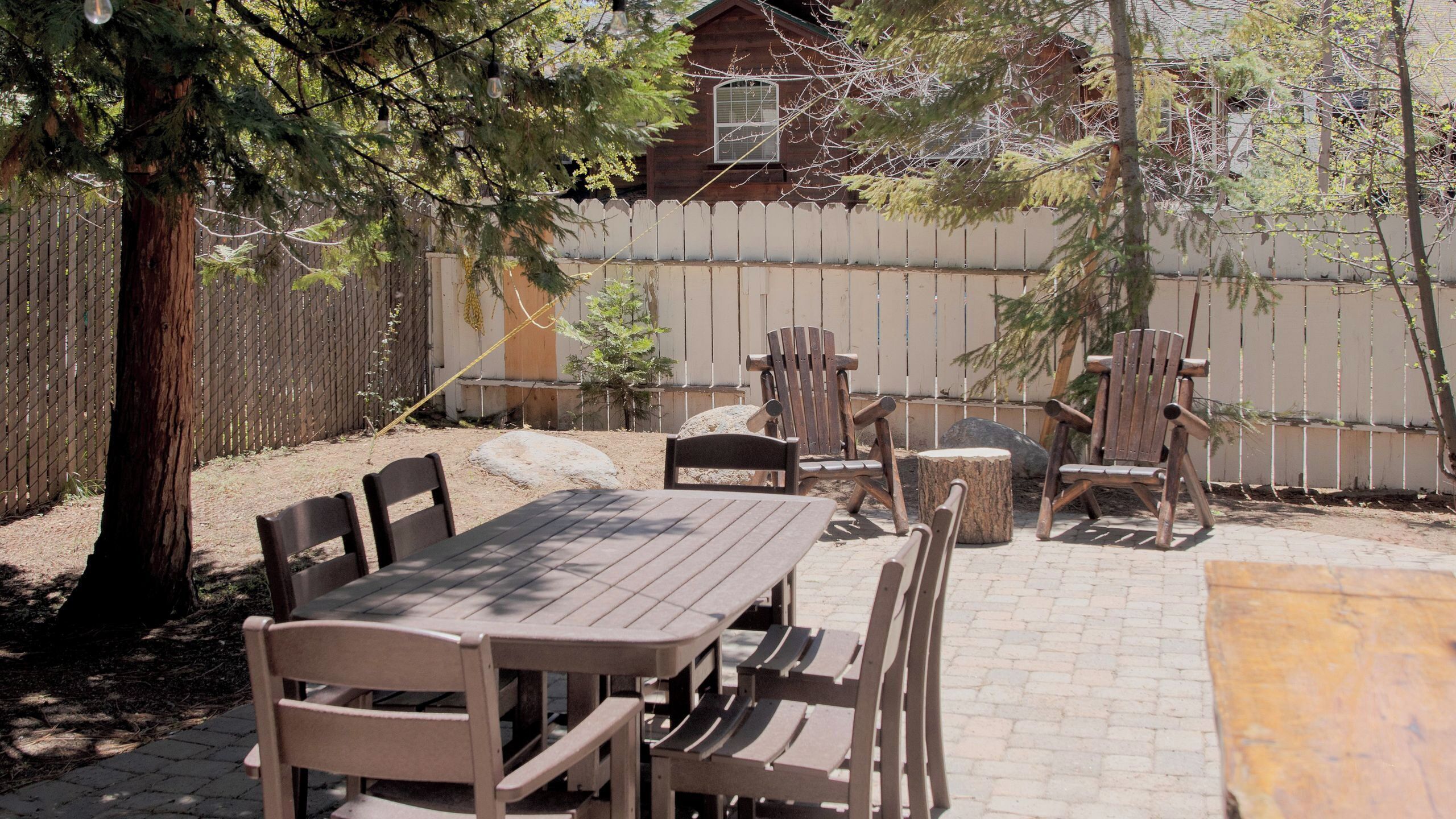 Une terrasse extérieure avec une table et des chaises en bois, une clôture en bois et un petit bâtiment en arrière-plan.