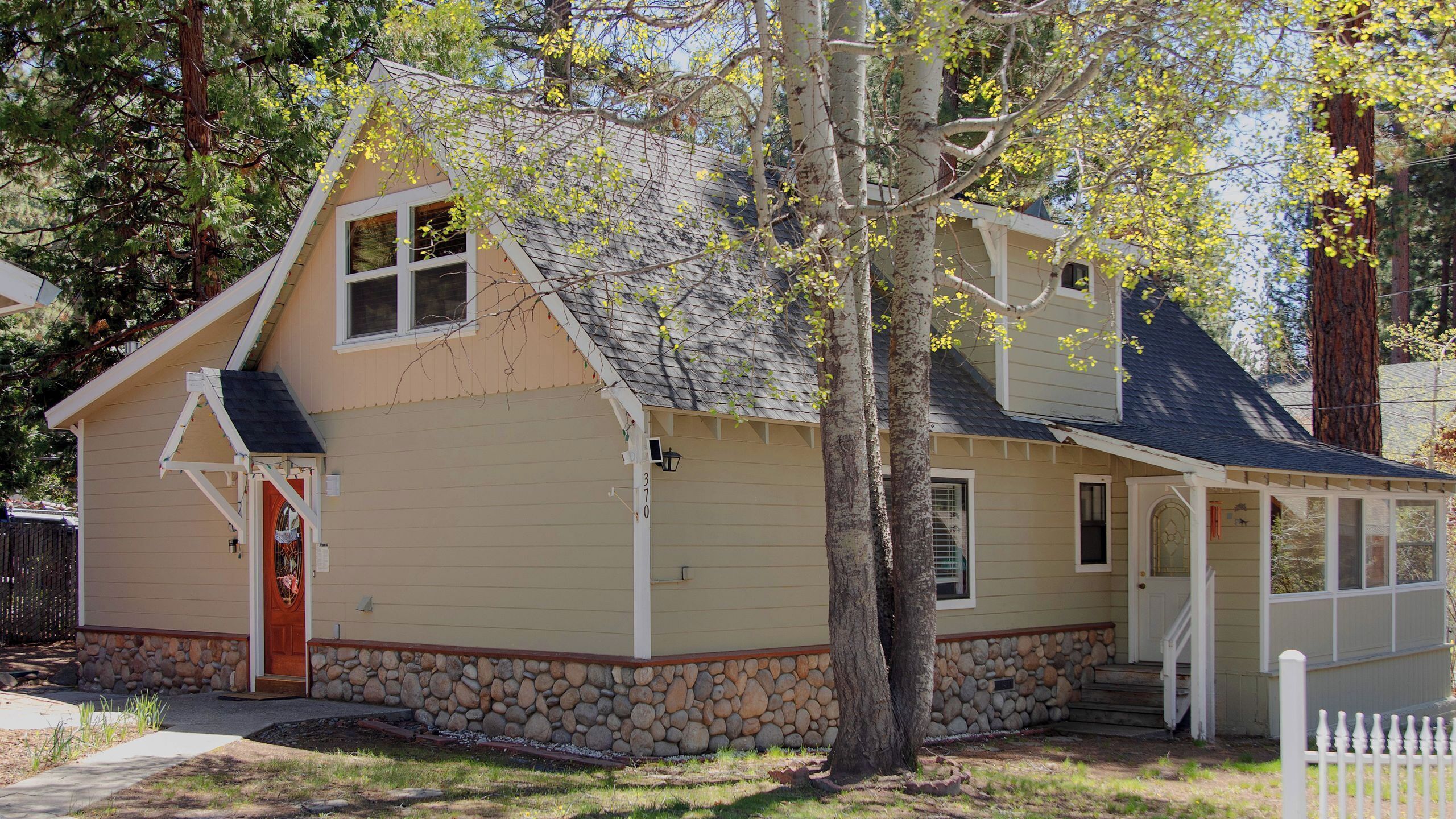 A single-story house with a stone foundation, a red door, and a porch.
