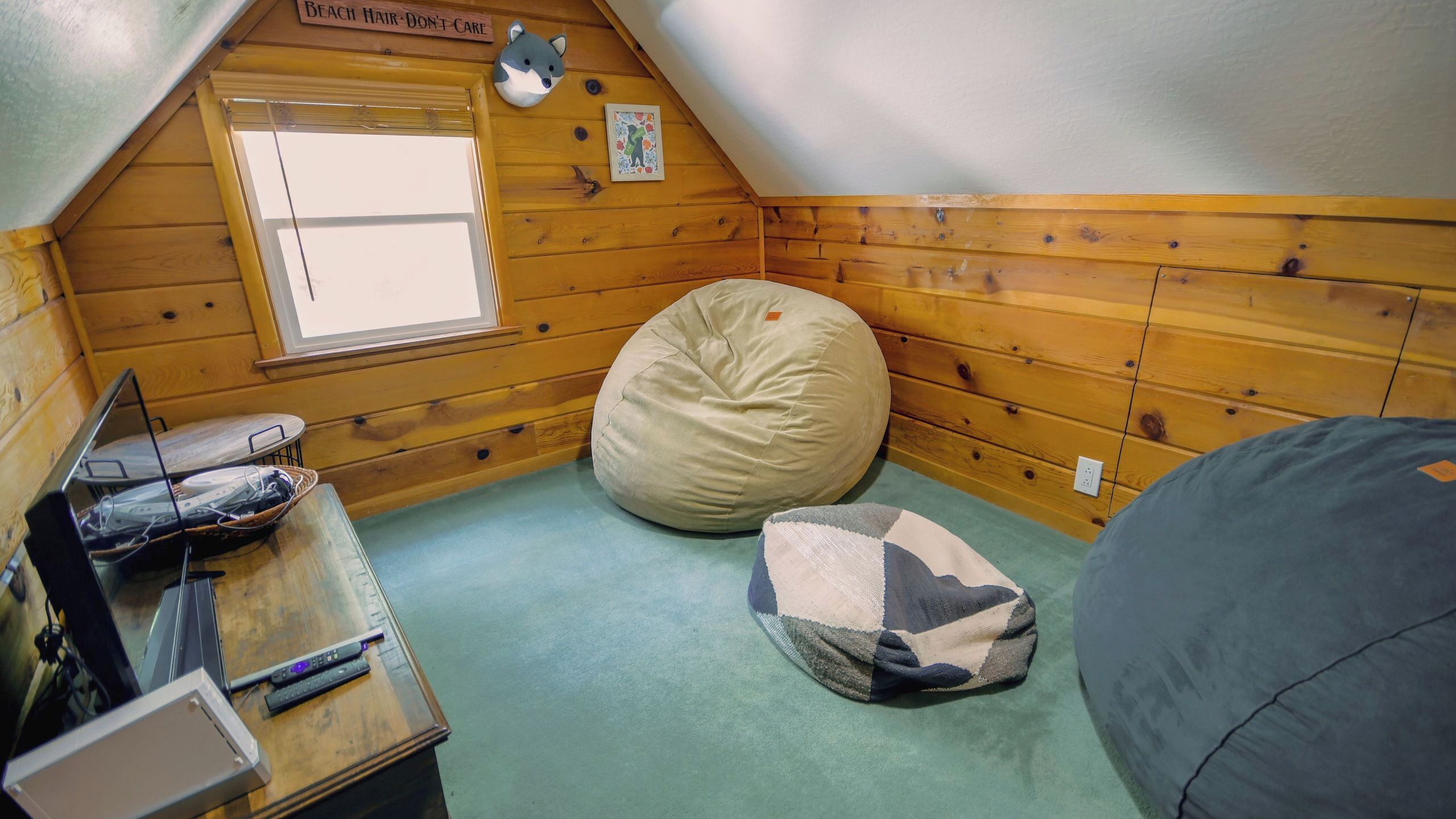 Een kleine, knusse kamer met houten wanden, een raam, een relax fauteuil, een bureau met een laptop en een aan de muur hangend schilderij.