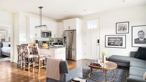 A modern kitchen with white cabinets, a stainless steel refrigerator, and a microwave. There is a dining area with a table and chairs, and a living room with a sofa and a coffee table. - Hart Suite Buyout 3 by Avantstay Two Town House Buyout w/ Modern Amenities in Nashville! (Nashville)