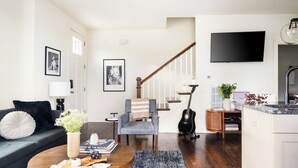 A modern living room with a sofa, a chair, a coffee table, a bookshelf, a guitar, and a staircase. - Hart Suite Buyout 3 by Avantstay Two Town House Buyout w/ Modern Amenities in Nashville! (Nashville)