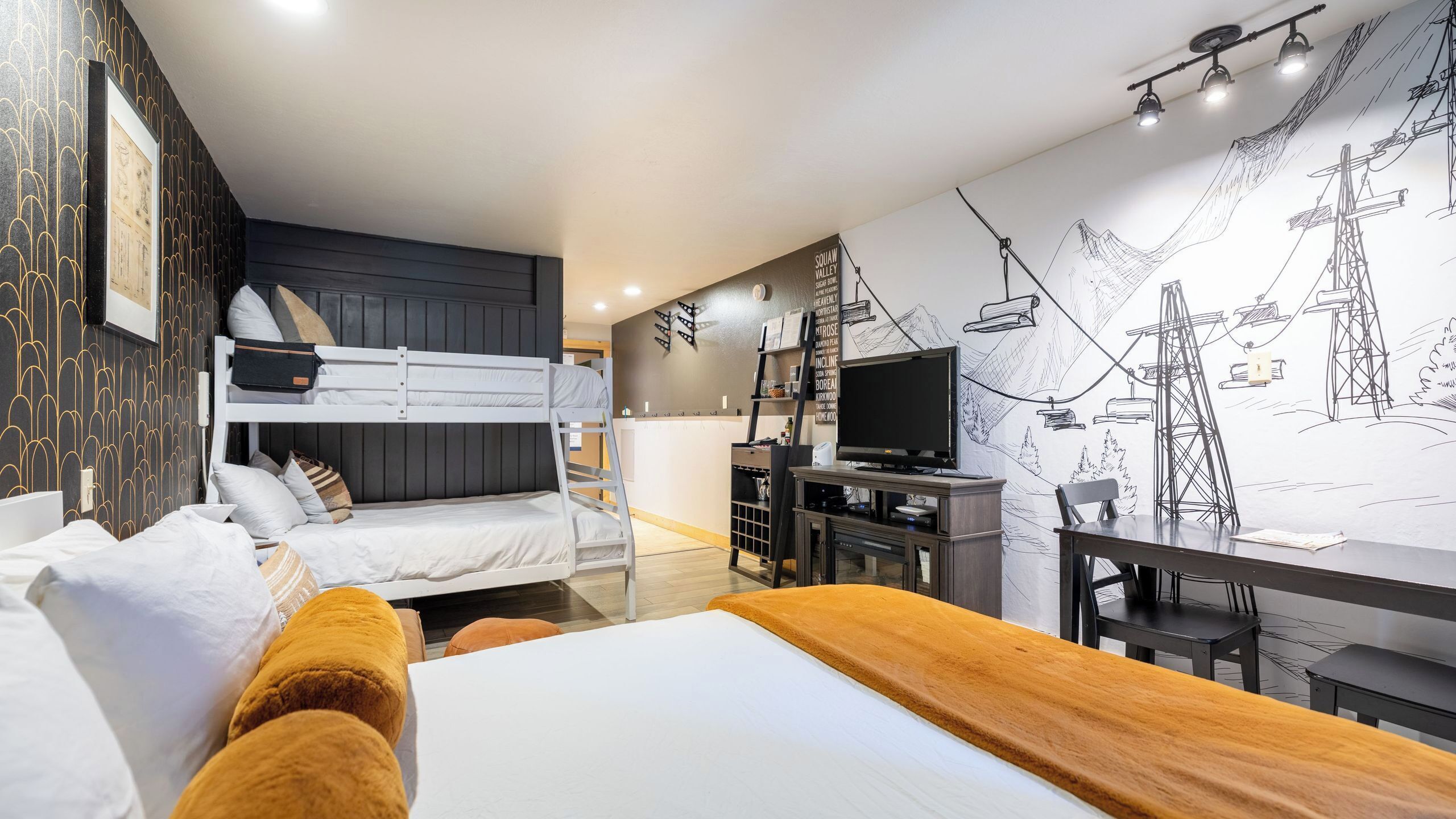 A modern hotel room with a bunk bed, a desk with a computer, a TV, and a mural on the wall.