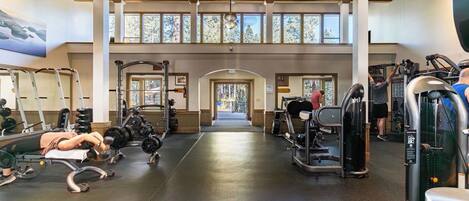 Et fitnessrum med træningsudstyr, løbebånd og et stort vindue med udsigt til træer.