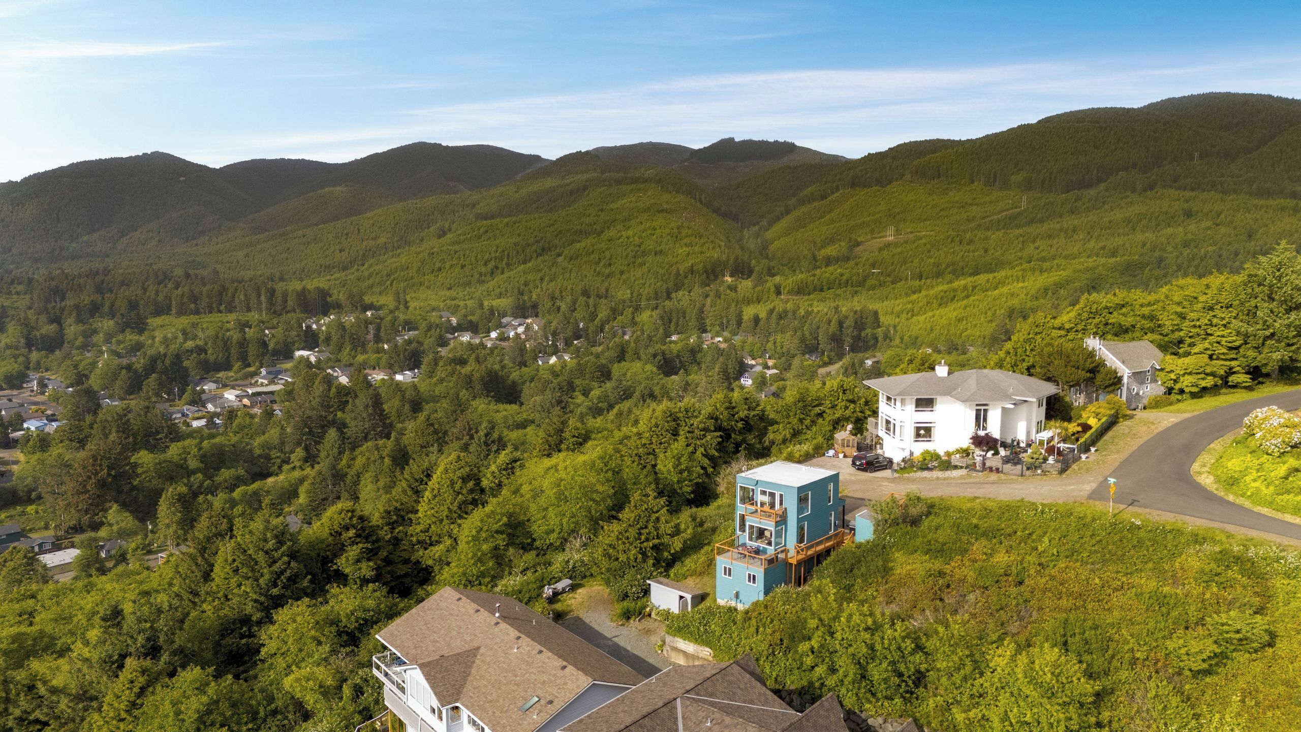 A residential area with houses surrounded by dense forests and hills.