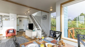 A modern kitchen with a built-in oven, a dining area with a table set for breakfast, and a staircase leading to a balcony with a view of greenery. - Blue Horizon by Avantstay Panoramic Views of the Ocean w/ Entertainers Patio (Rockaway Beach)