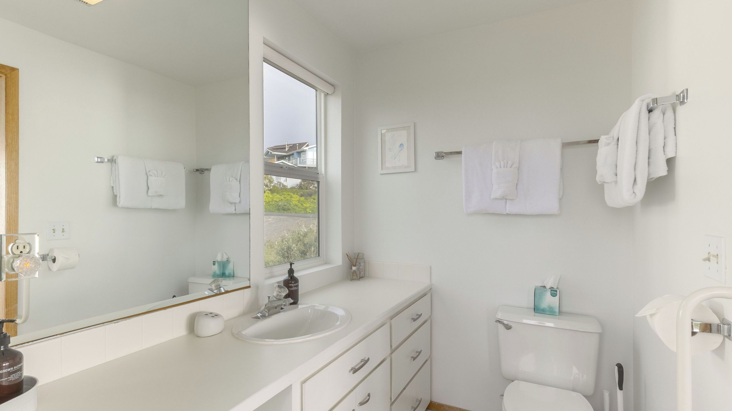 Un baño moderno con un espejo grande, un lavamanos, un inodoro y una ventana.