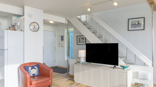 A modern living room with a sofa, a flat-screen TV, a staircase, and a dining area. - Blue Horizon by Avantstay Panoramic Views of the Ocean w/ Entertainers Patio (Rockaway Beach)