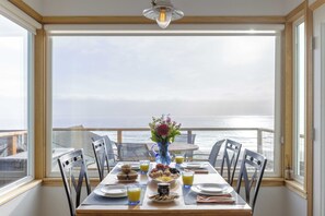 A dining table with breakfast items and a vase of flowers, overlooking a scenic ocean view. - Blue Horizon by Avantstay Panoramic Views of the Ocean w/ Entertainers Patio (Rockaway Beach)