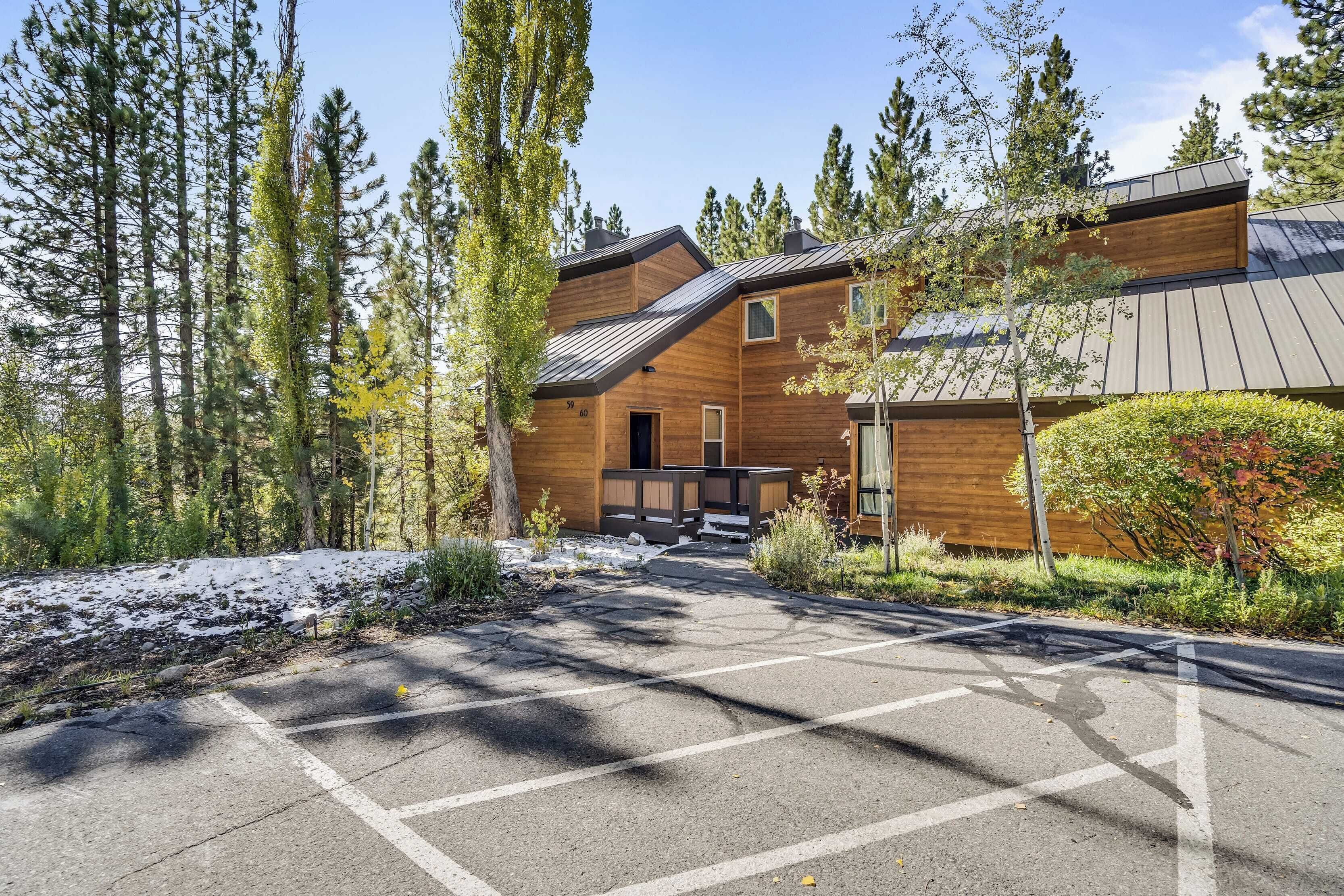 A modern building with a wooden exterior, surrounded by tall trees and a parking area.