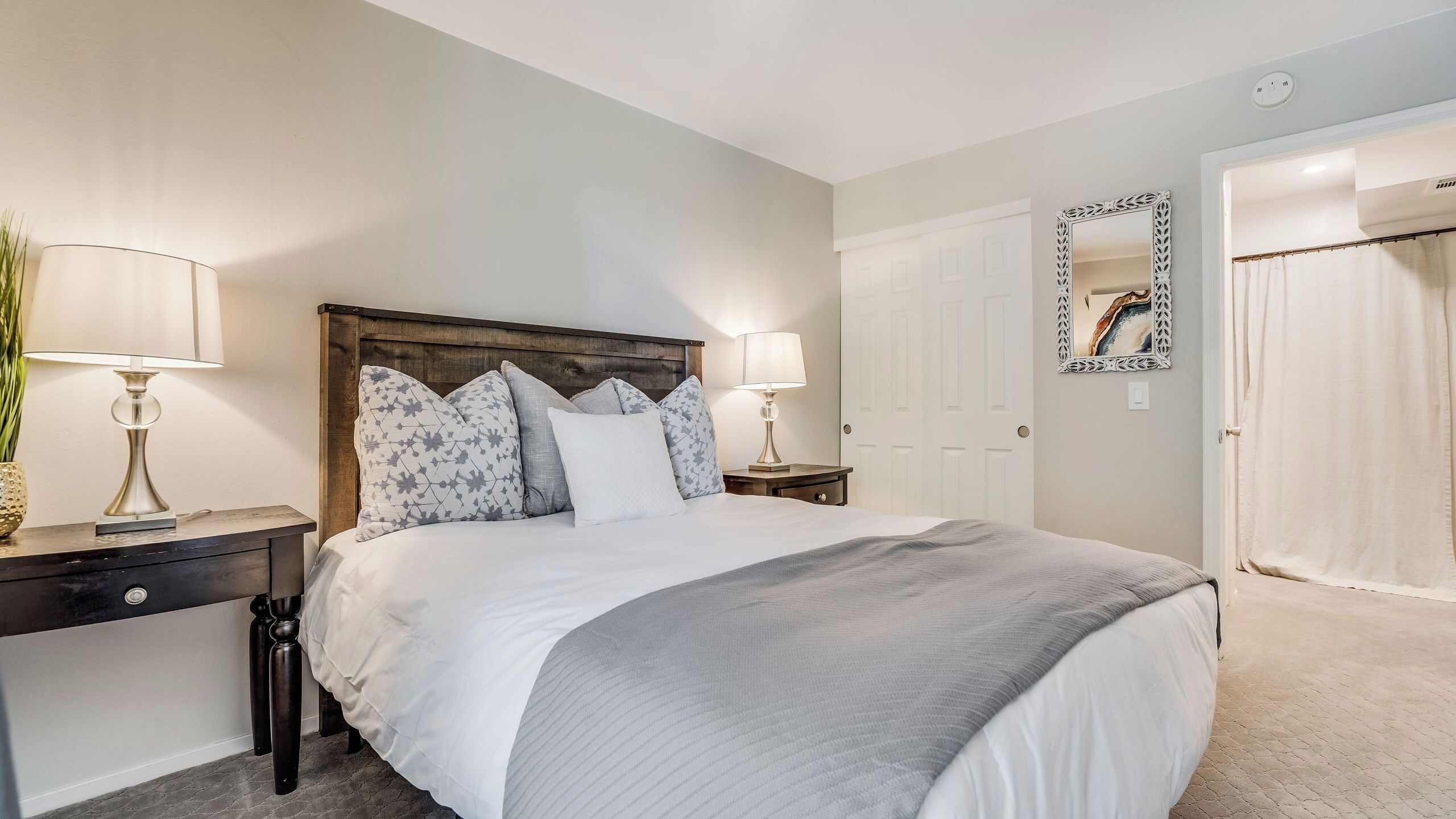 A neatly arranged bedroom with a bed, bedside tables, a mirror, and a door.