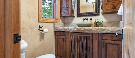 A bathroom with wooden cabinets, a white toilet, a sink with a mirror above it, and a window providing natural light.