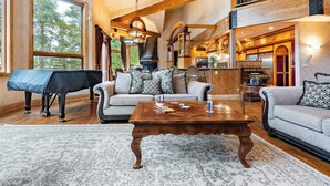 A spacious living room with a piano, two sofas, a coffee table, and a large window.